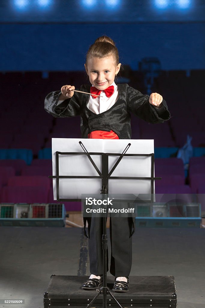 Music conductor conducting orchestra Happy little girl music conductor conducting the orchestra standing in front of the conductor's stand in a concert hall Girls Stock Photo