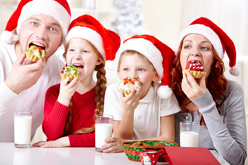 Cheerful family in Santa hats eating delicious pastry