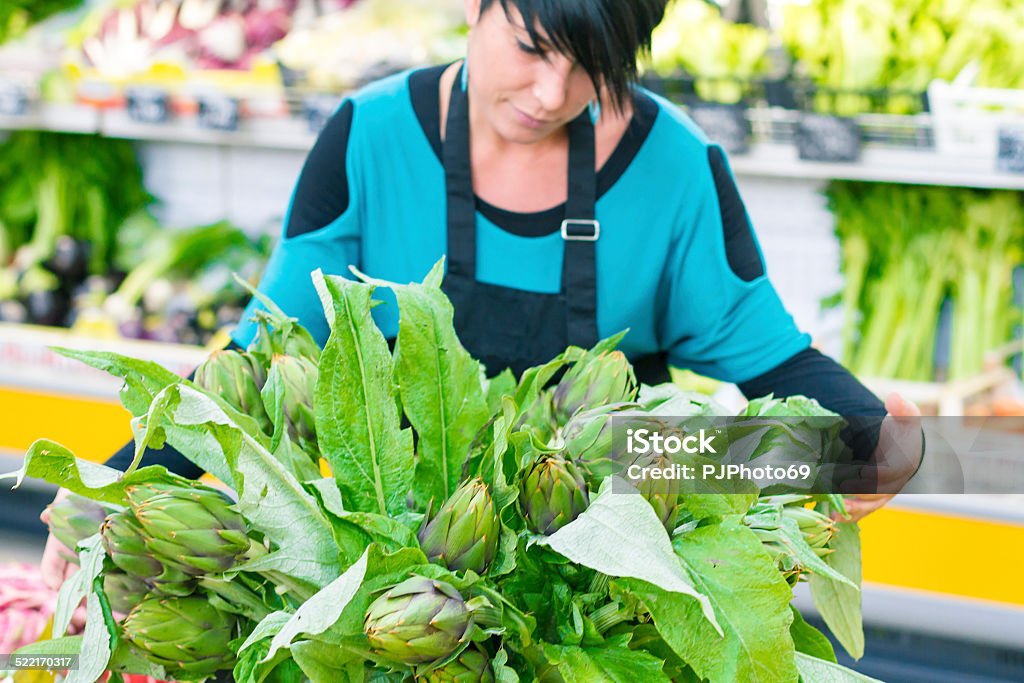 Young woman with Bunch of artichokes Young woman (shop assistant or owner 30 years old with short black hair and nose-ring) working on Bunch of artichokes in a supermarket - Selective focus 30-39 Years Stock Photo