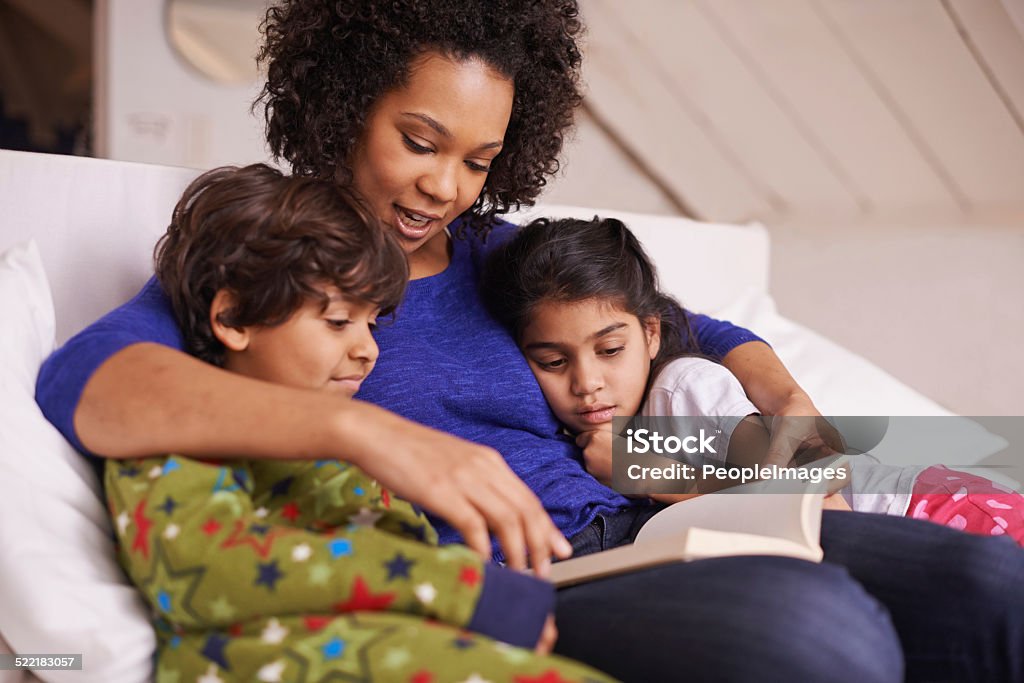 And then they lived happily ever after... A young mother reading to her children while relaxing at home Bedtime Stock Photo