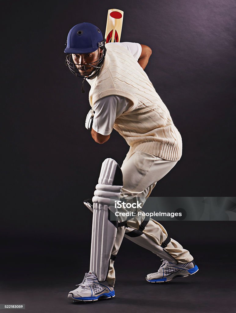 The perfect strike A cropped shot of an ethnic young man in cricket attire isolated on black Sport of Cricket Stock Photo