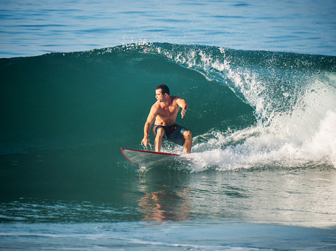 Young man surfing and trying to catch pipeline wave.