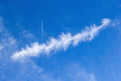 A commercial airplane is darting in the sky. There is a unique cloud under it.