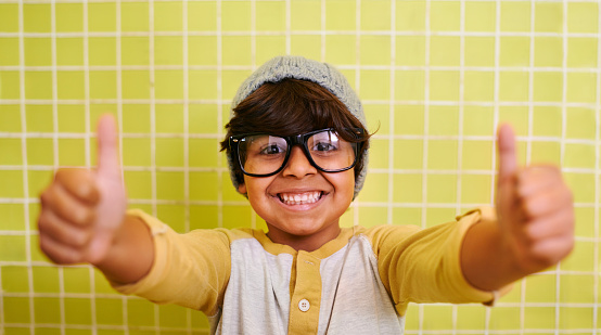 Shot of a cute little boy wearing glasses and a beanie showing thumbs up