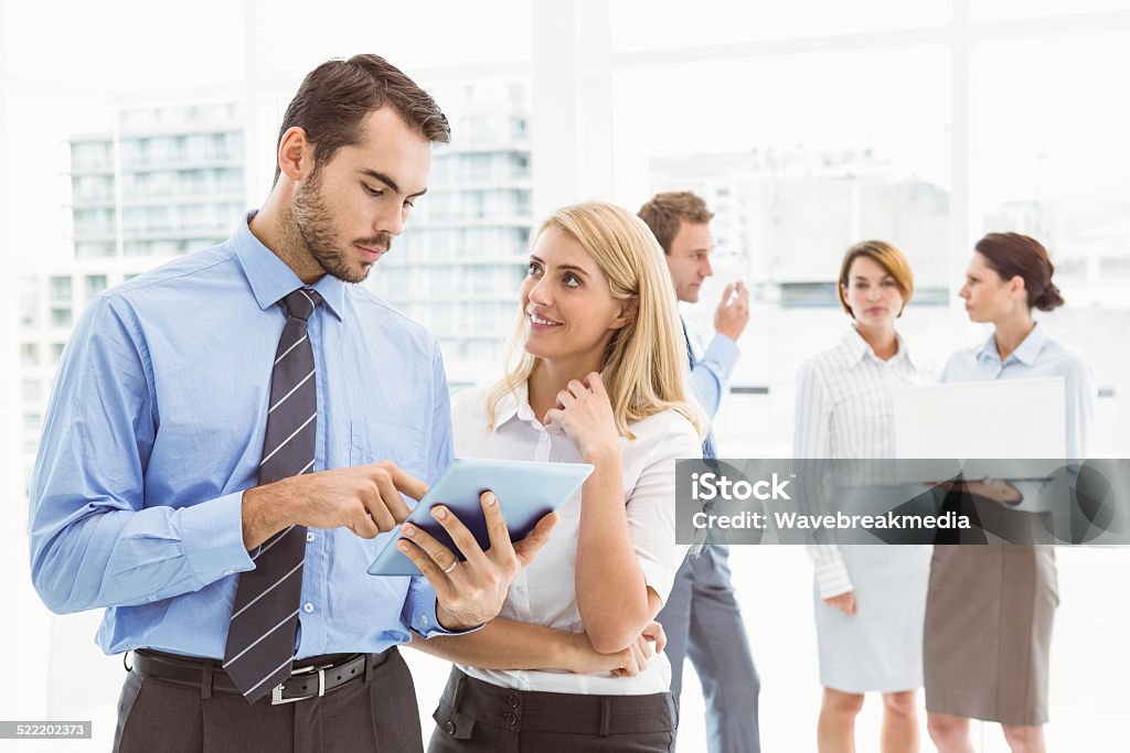 Business couple using digital tablet with colleagues behind Business couple using digital tablet with colleagues behind in office 20-29 Years Stock Photo