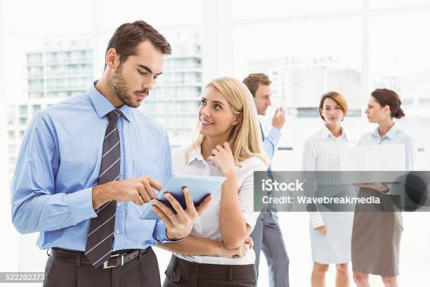 Business Couple Using Digital Tablet With Colleagues Behind Stock Photo - Download Image Now