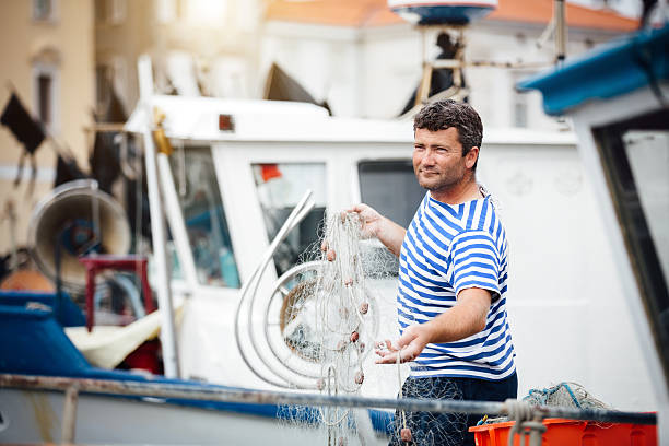Local fisherman in a white and blue striped shirt preparing his nets on a dock. Boat in a background.