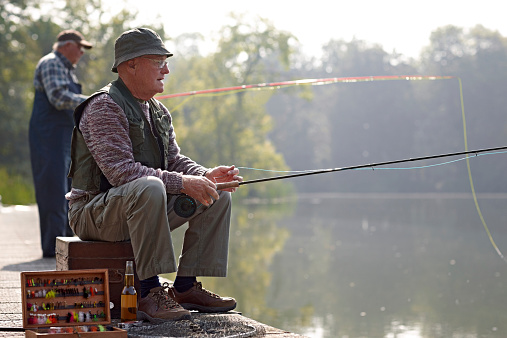 Relaxed senior fisherman fishing from the dock in river with a fishing rod