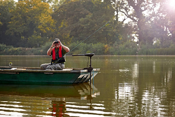 istock Senior man in a small boat looking through binoculars 522222373