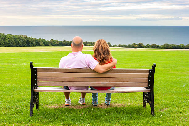 Rear view of middle age couple sitting on a bench looking at the sea