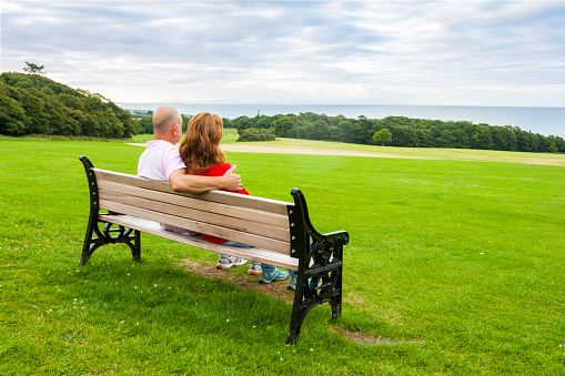 Rear view of middle age couple sitting on a bench looking at the sea