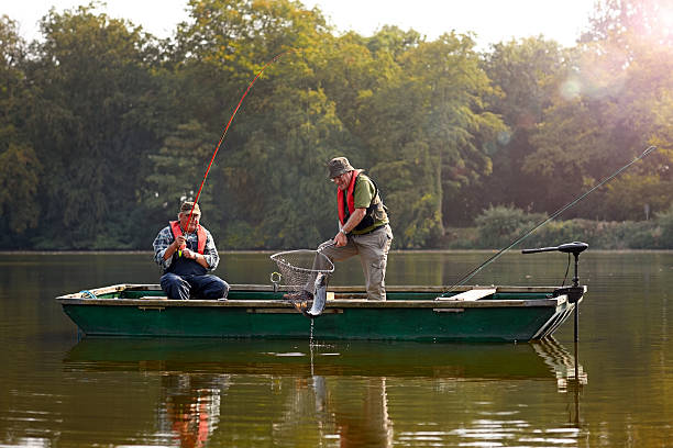Two senior man catching fish Two senior man catching fish with fishing rod and net on a lake fishing boat photos stock pictures, royalty-free photos & images
