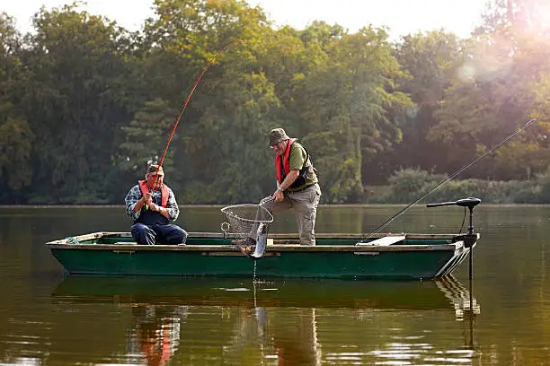Two senior man catching fish with fishing rod and net on a lake