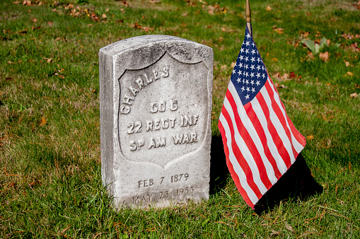 Weymouth, MA, USA-November 3, 2014: Veterans are due honors, and even veterans from long ago fought wars are honored on Veterans 'Day. Here, a simple granite gravestone and an American flag mark the grave of a Spanish American War veteran/