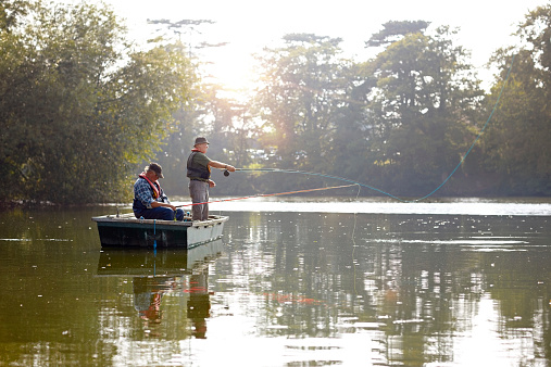 Two senior men in a boat fly fishing on a sunny day