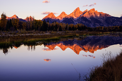 Beautiful reflection of Grand Teton mountain range in Snake River waters on a fine autumn morning as viewed from Schwabachers Landing in Grand Teton National Park, Wyoming, USA with first light hitting the mountain peaks