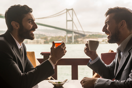 Business meeting over coffee and tea in Istanbul. Two smiling businessmen meet with view of Bosphorous Bridge, Istanbul, Turkey