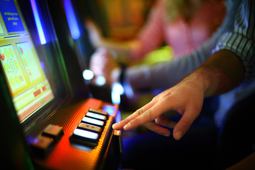 Closeup of unrecognizable caucasian man making money on  slot machine in casino. He's playing slot poker. There are blurry people in background also playing.