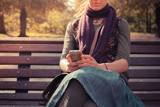istock Young woman on park bench using her phone 522277605