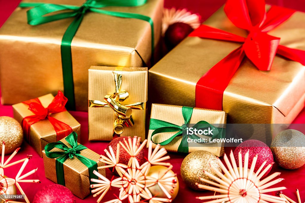 Six Golden Xmas Presents with Bows Six Christmas gifts all wrapped in gold. Bows in red and green also. Placed next to straw stars and ornaments on a red cloth. Shallow depth of field with focus on wide emerald bow around golden box. Box - Container Stock Photo