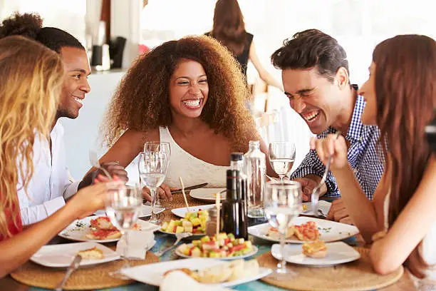 Group Of Young Friends Enjoying Meal In Outdoor Restaurant Laughing