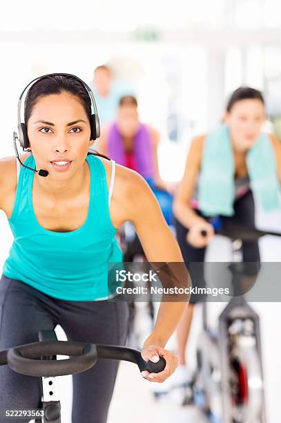 Instructor Wearing Headset Cycling With Customers At Gym Stock Photo - Download Image Now