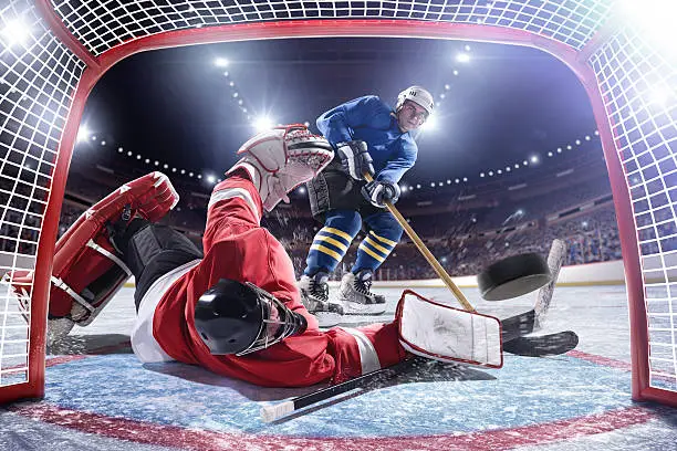 Inside gates view  of professional ice hockey player scoring during game in indoor arena full of spectators.