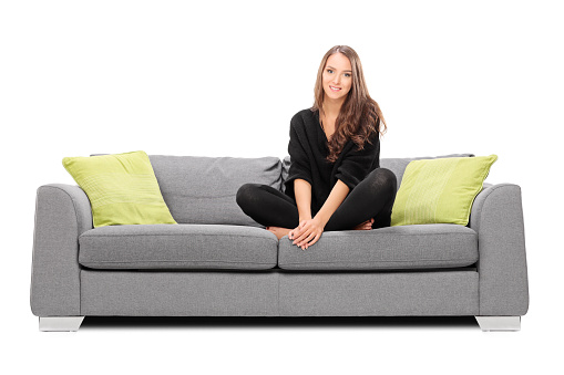 Young woman sitting on a sofa and looking in the camera isolated on white background