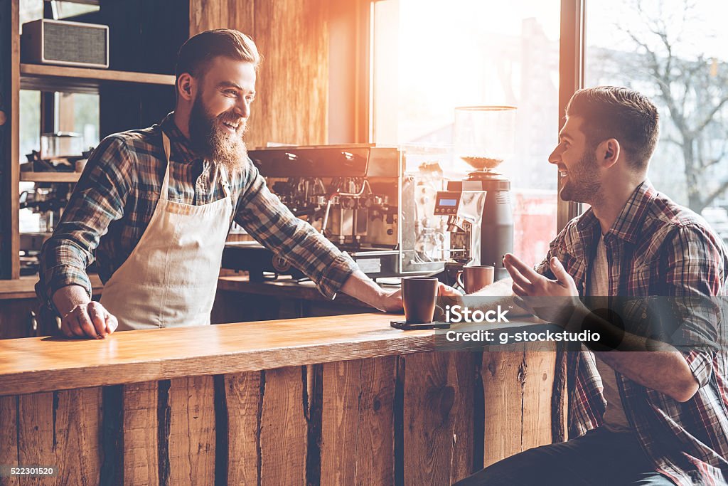Good talk with customer. Barista and his customer discussing something with smile while sitting at bar counter at cafe Customer Stock Photo