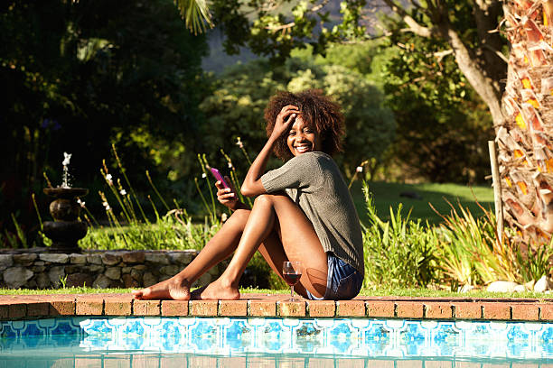 istock Smiling young woman with cellphone sitting by pool 522305210