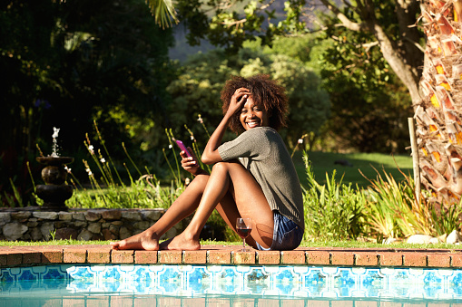 Portrait of a smiling young woman with cellphone sitting by pool