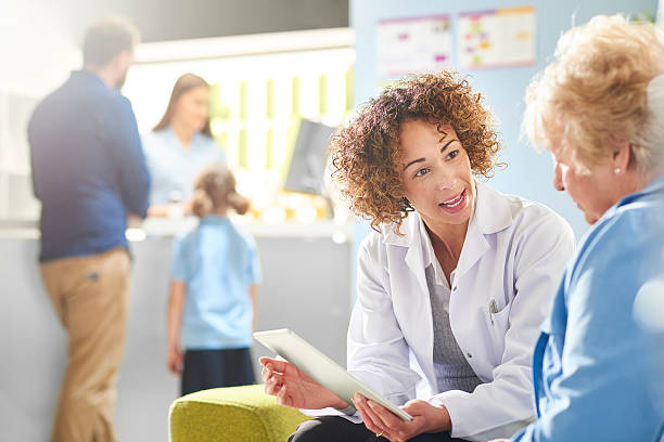 pharmacist advice A female pharmacist sits with a senior female patient in the pharmacist consultation area and discusses her prescription and choice of medication. In the background a father and daughter stand at the dispensing counter and are served by a female pharmacy assistant . lens flare offspring daughter human age stock pictures, royalty-free photos & images