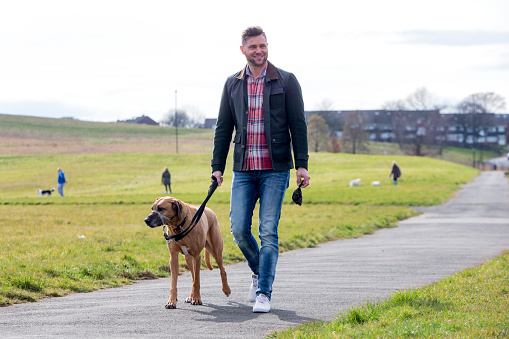 An attractive young male is walking in a field with his dog.