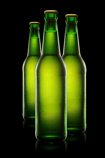 Three green wet bottles of beer on black background.