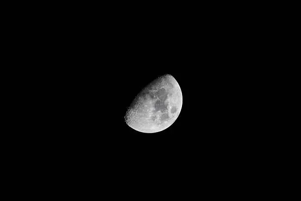 First Quarter Moon Phase - View of lunar features through an astronomical telescope in the dark night sky