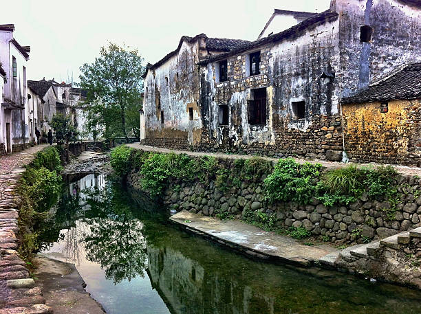 Longmen, Zhejiang, China - November 15, 2012: This image captures a typical street scene if you were to walk through a traditional Chinese river town. The decaying Ming and Qing dynasty buildings line the narrow alleyways. The fading whitewash and crumbling buildings give a distinctive old ancient cultural style feel to the village.