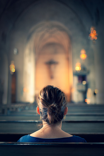 A woman sitting in a bench row in a large old christian church.