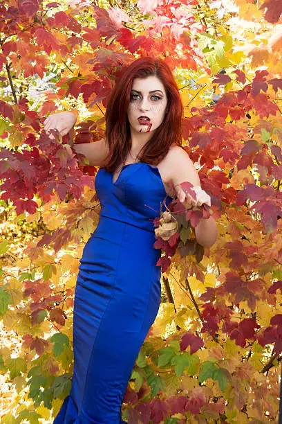 Photo of Redheaded teen vampire in blue dress, against colourful Autumn shrub.