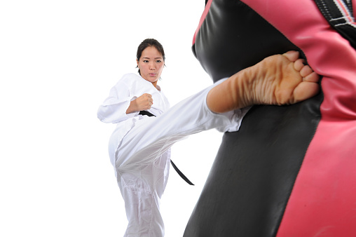 Asian female kicking a padded focus shield with a powerful roundhouse.