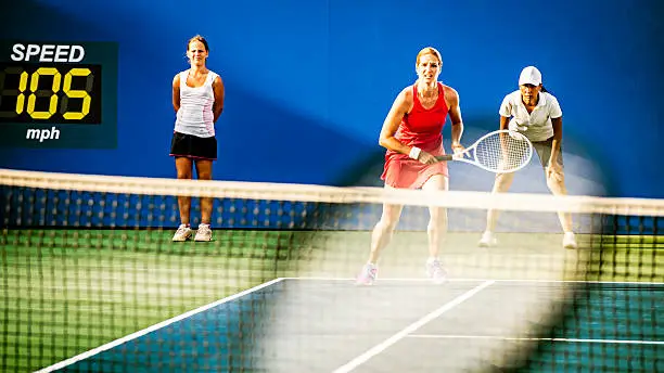 Female tennis player running towards the ball, line judge and ball girl in the background, a blurred tennis racket in the foreground .