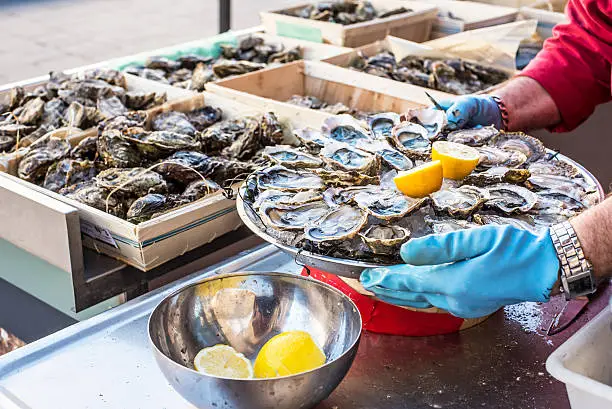 Tray of opened fresh oysters on half shell on ice with lemon in a street of Bordeaux, capital of Aquitaine. France.