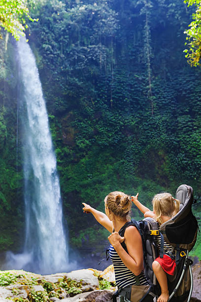 istock Mother with child in backpack looking at jungle waterfall 522317662