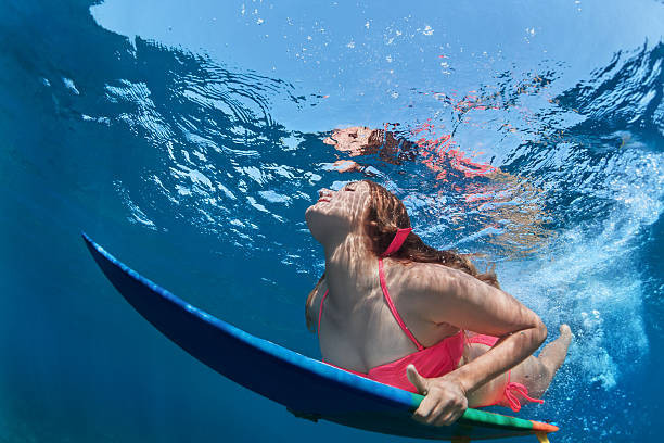 istock Surfing girl with board dive under ocean wave 522317990