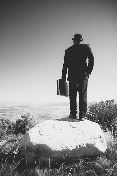 Old fashioned businessman carries a suitcase on top of a boulder