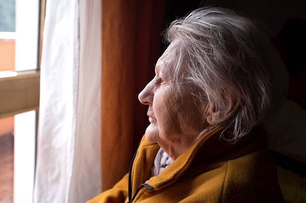 vieille femme regardant dans une fenêtre - fragilité photos et images de collection