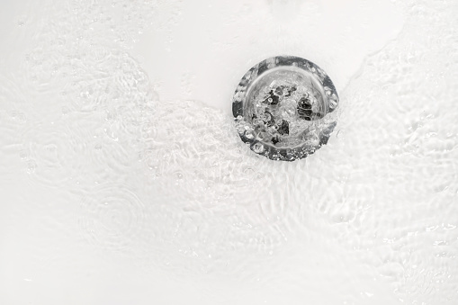 White bathroom sink drain close up with water ripple and bubbles