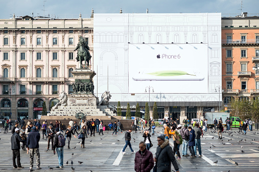 Milan, Italy - November 4, 2014: People walking in Piazza Duomo in front of a large Apple iPhone 6 billboard in Milan city centre