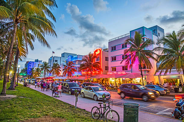 people enjoy palms and art deco hotels at Ocean Drive Miami, USA - August 23, 2014: people enjoy Palm trees and art deco hotels at Ocean Drive by night. The road is the main thoroughfare through South Beach in Miami, USA. south beach photos stock pictures, royalty-free photos & images