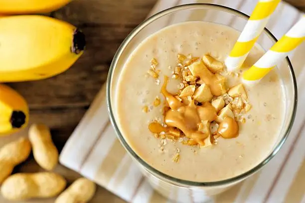 Peanut butter banana oat smoothie with paper straws close up, downward view with cloth