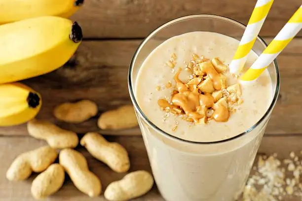 Peanut butter banana oat smoothie with paper straws on rustic table with scattered ingredients